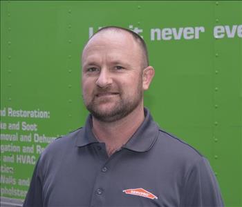 Male employee with beard wearing a gray shirt with a green background.